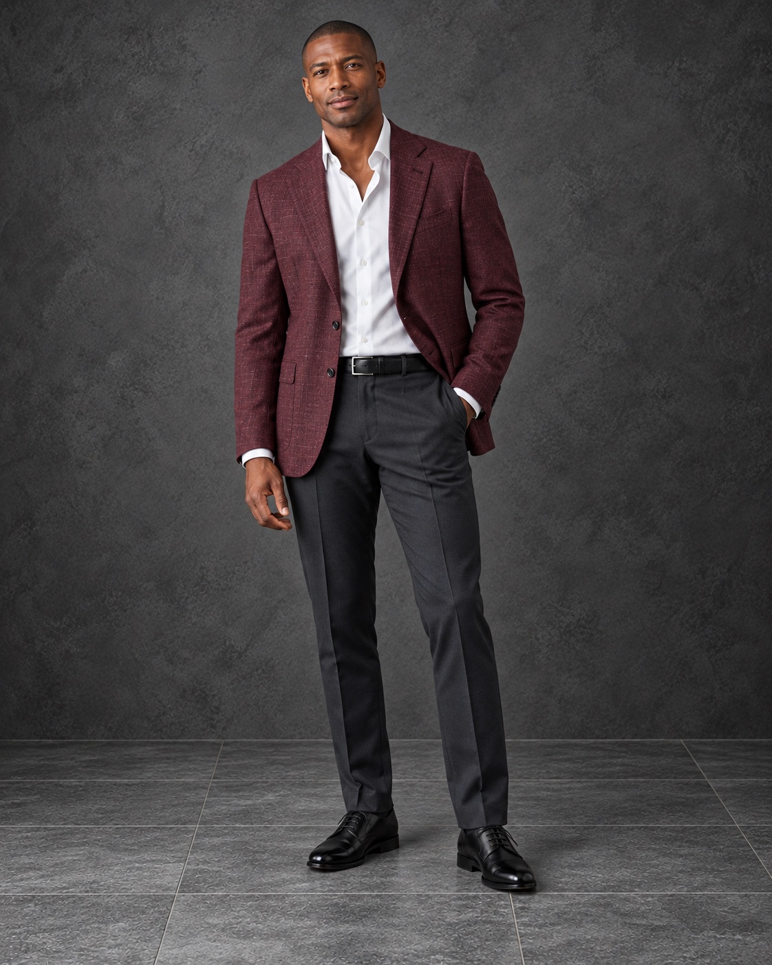 A man wearing a burgundy textured sport coat, white shirt, charcoal tailored trousers, black leather belt, and black dress shoes